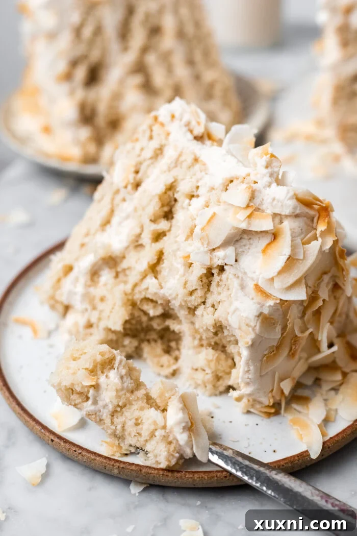 A beautifully sliced vegan coconut cake, revealing moist layers and creamy frosting, topped with toasted coconut flakes.