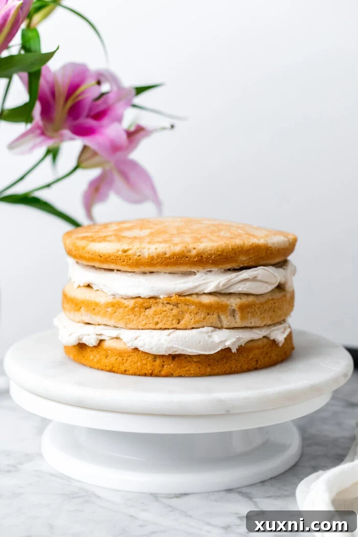 A vegan coconut cake being assembled and frosted with dairy-free coconut cream cheese frosting, showing the layering process.