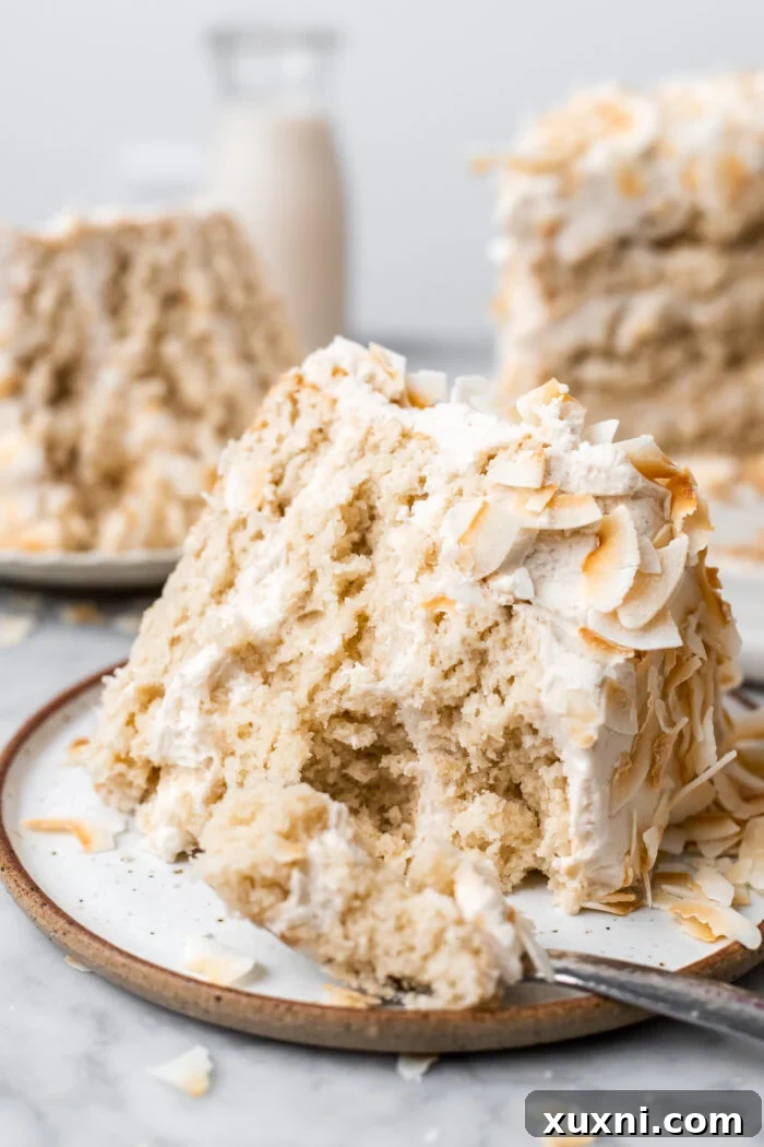 A bitten slice of vegan coconut cake, showing the perfect texture and tempting frosting, on a plate.