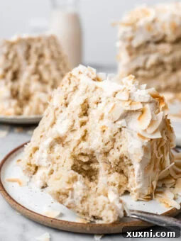 A delicious bite taken out of a slice of vegan coconut cake, highlighting its moist interior and creamy frosting.