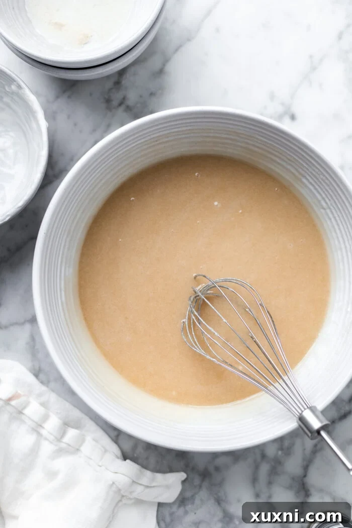 Hands mixing vegan coconut cake batter in a bowl, illustrating the 'by hand' method.
