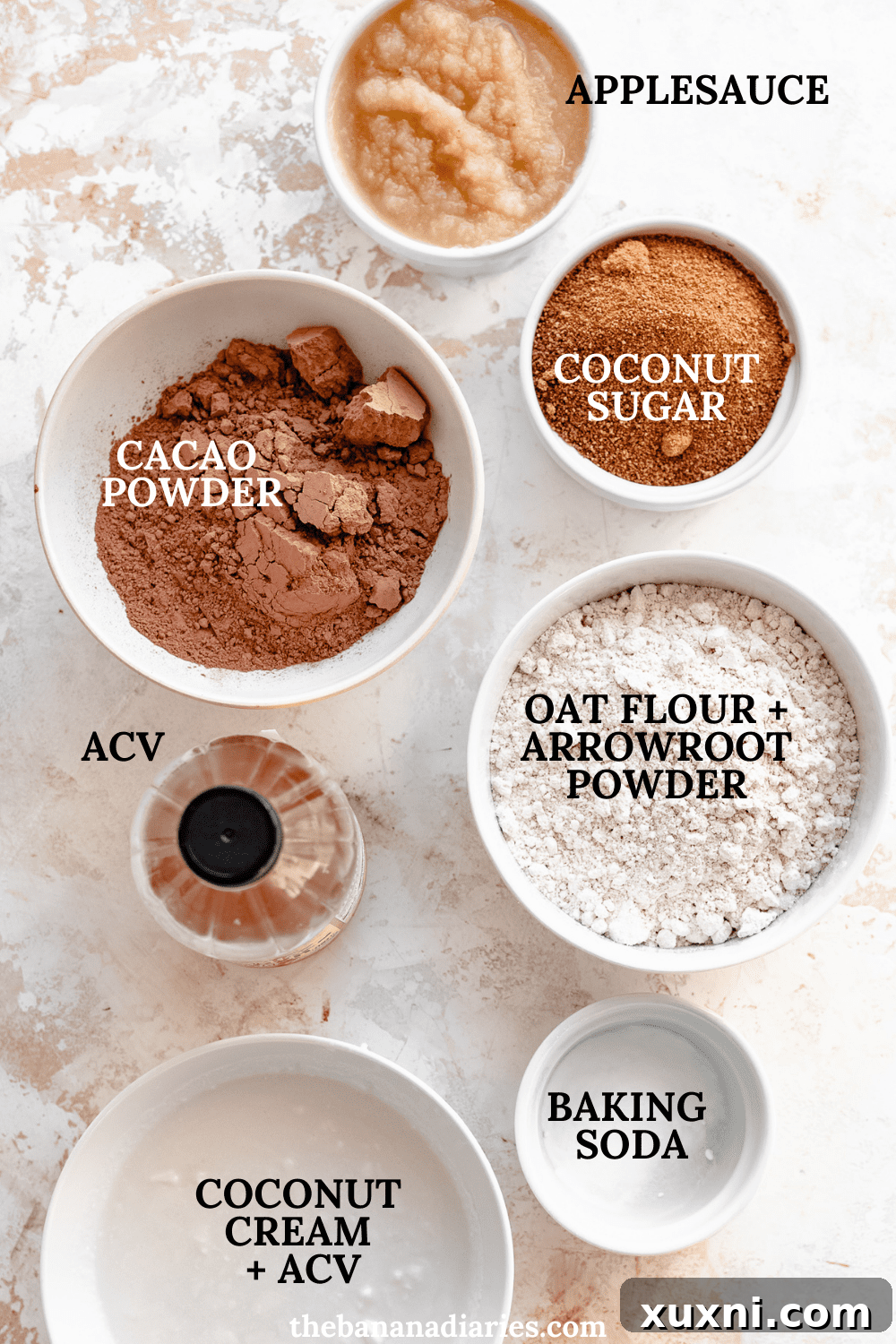 Arrangement of vegan sheet cake ingredients including oat flour, cacao powder, coconut sugar, applesauce, and dairy-free milk.