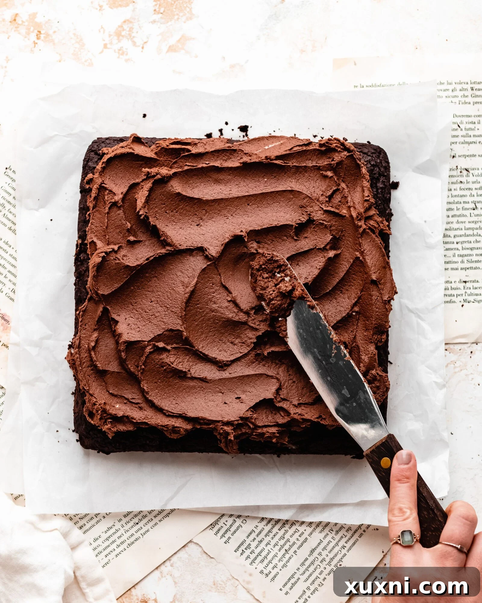 Frosting being applied smoothly onto the cooled vegan half sheet cake.