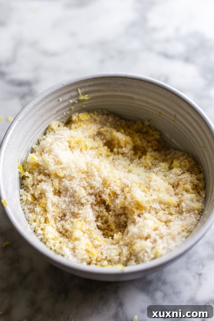 Zesty & Moist One-Bowl Vegan Raspberry Lemon Sheet Cake with Tangy Lemon Curd 5 Lemon zest being rubbed into sugar in a mixing bowl, a crucial step for intense lemon flavor.