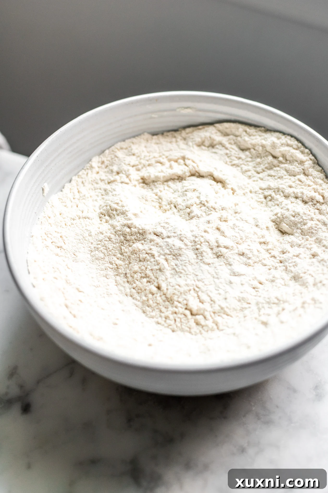A bowl of perfectly measured dry ingredients including flour, baking powder, sea salt, and a hint of nutmeg.