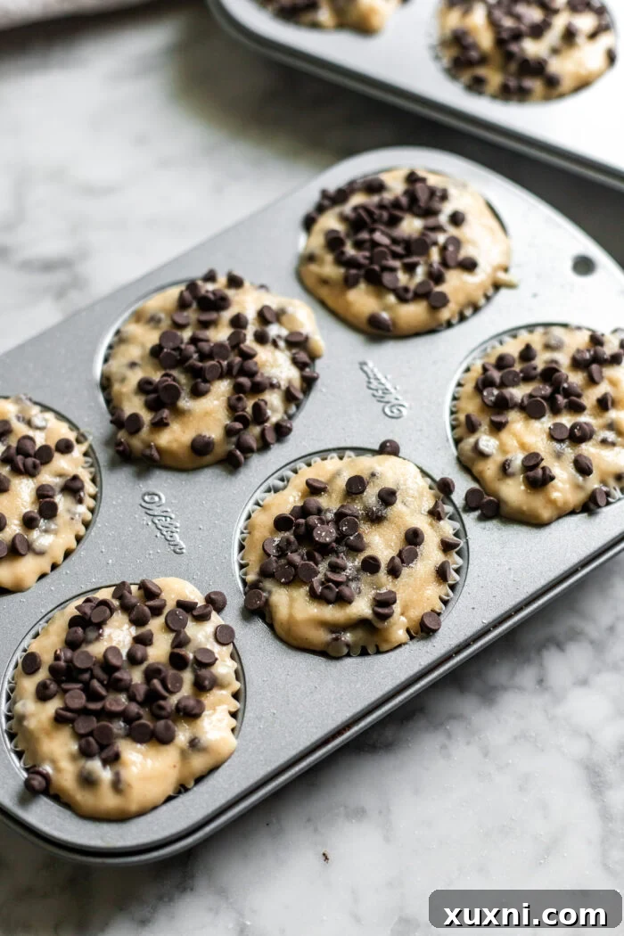 Muffin tin filled with unbaked vegan chocolate chip muffin batter, topped with extra chocolate chips and sugar.