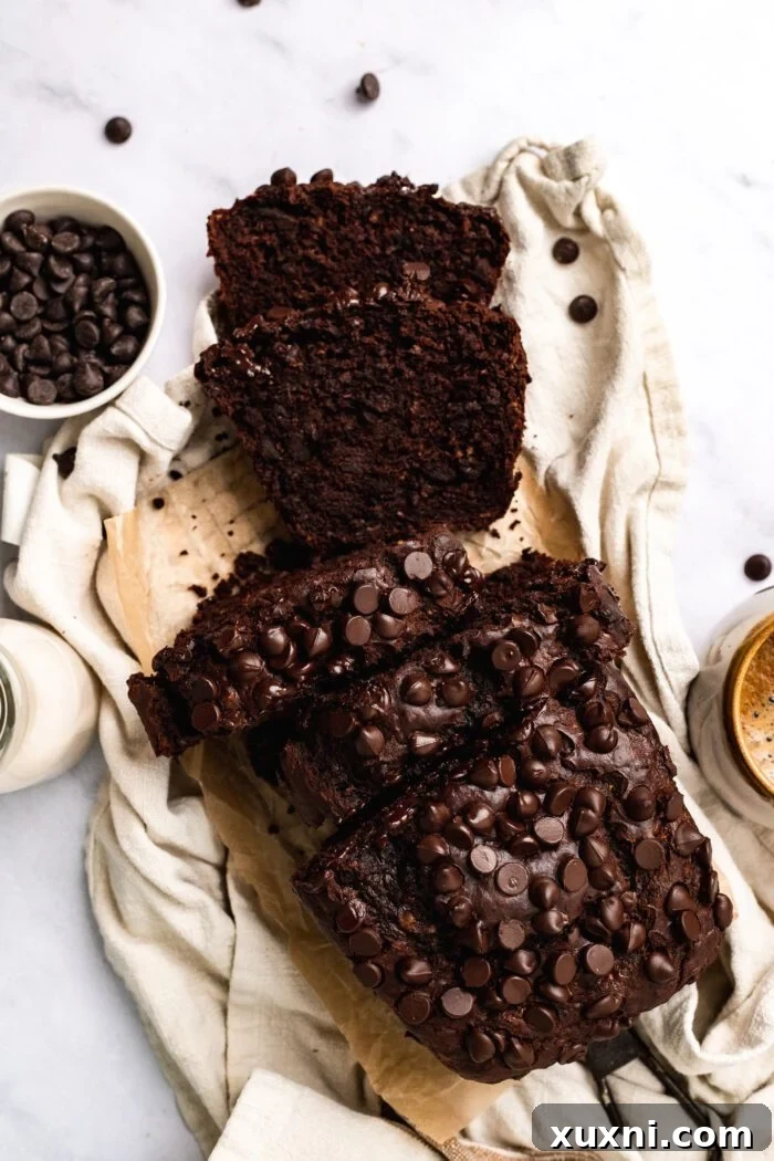 A perfectly sliced loaf of fudgy vegan chocolate banana bread on a rustic cloth, accompanied by a coffee mug and a sprinkle of chocolate chips, highlighting its rich texture and decadent appeal.