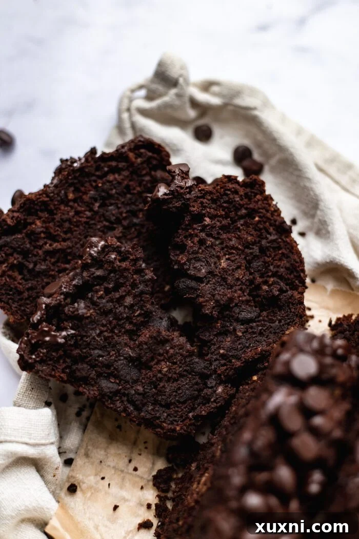 A close-up shot of a broken open slice of vegan chocolate banana bread, revealing its exceptionally moist, fudgy texture and abundant chocolate chips.
