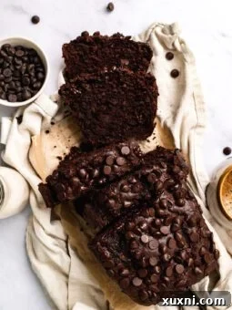 sliced vegan chocolate banana bread loaf on cloth with coffee mug and chocolate chips