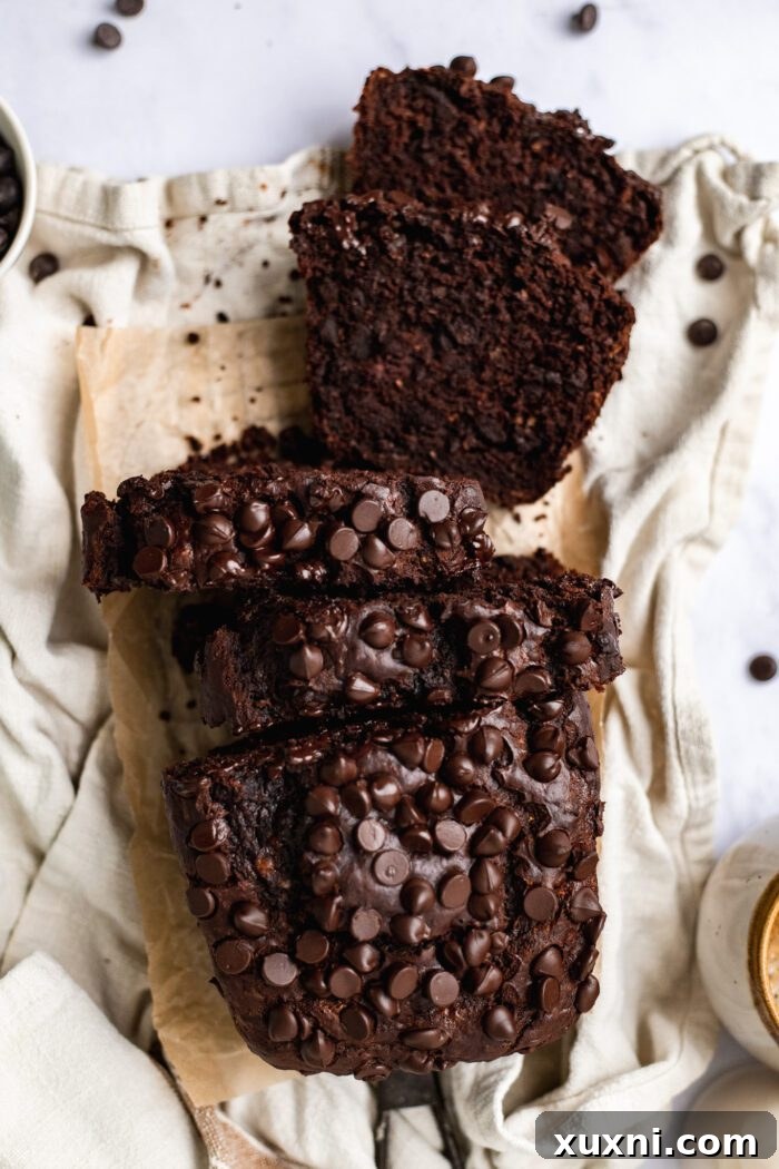 Several slices of rich vegan chocolate banana bread stacked elegantly, highlighting the dense, fudgy texture and abundant chocolate chips within each piece.