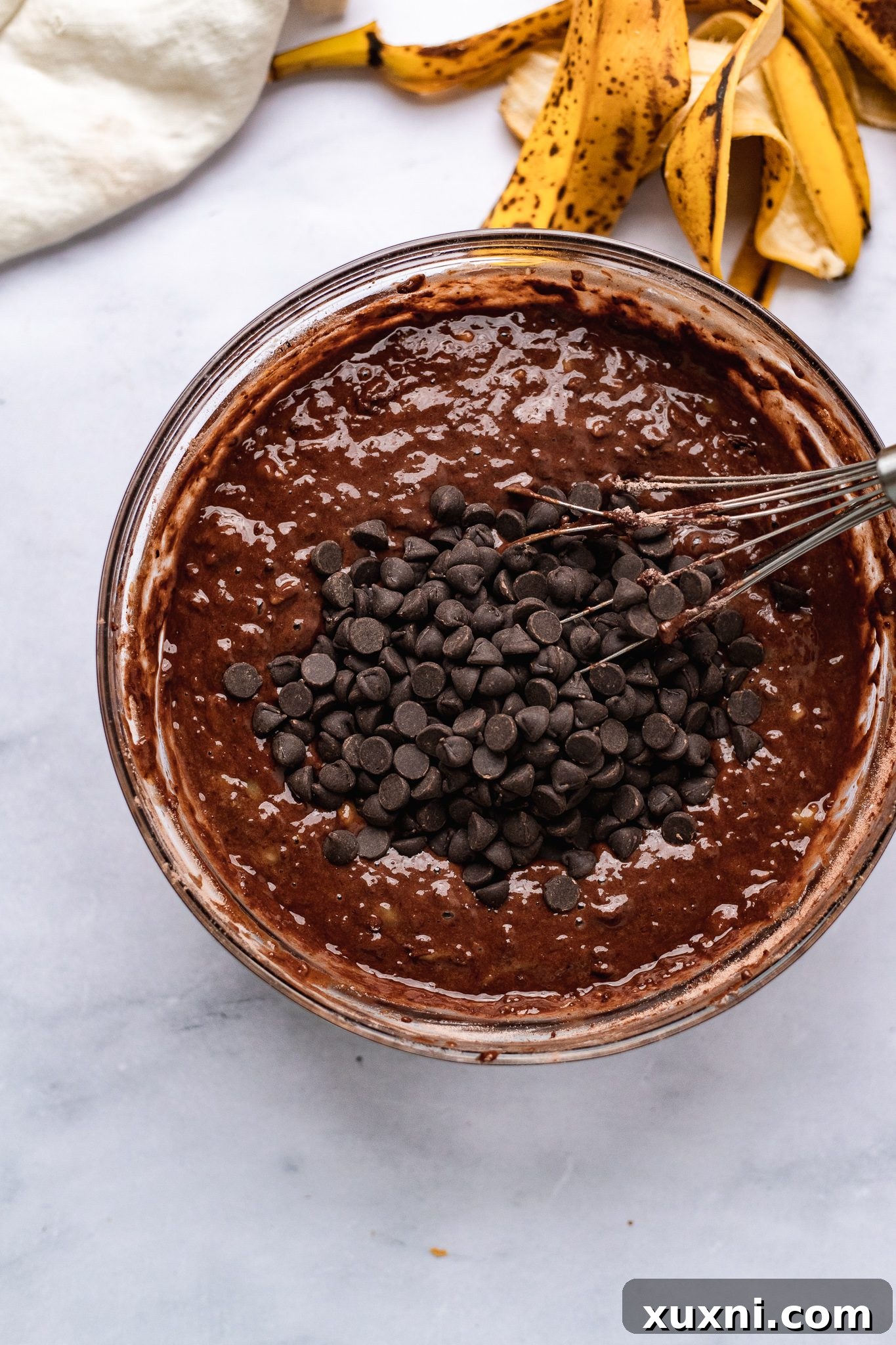 Close-up of the mixed vegan chocolate banana bread batter in a bowl, showing the rich, dark consistency and the addition of chocolate chips.