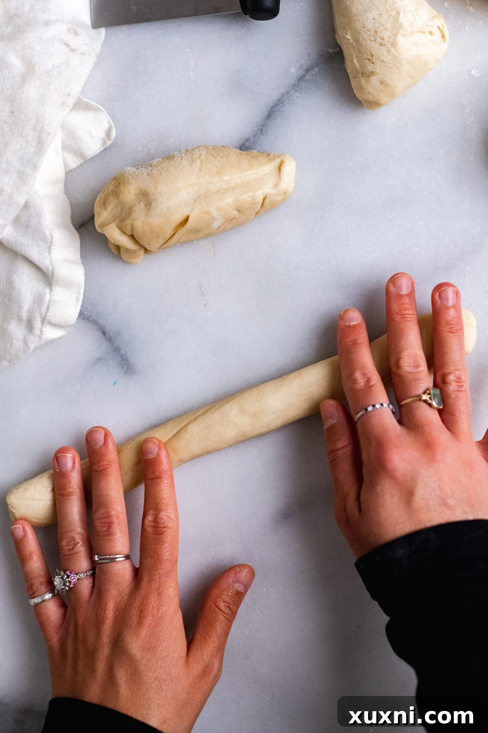 Hands skillfully rolling out a segment of vegan Easter bread dough into a long, even strand for braiding.