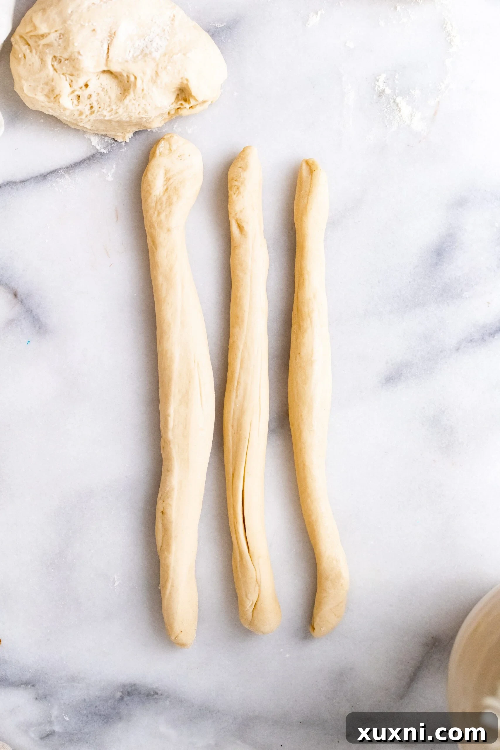 Three strands of vegan Easter bread dough neatly rolled out, poised for the braiding process.