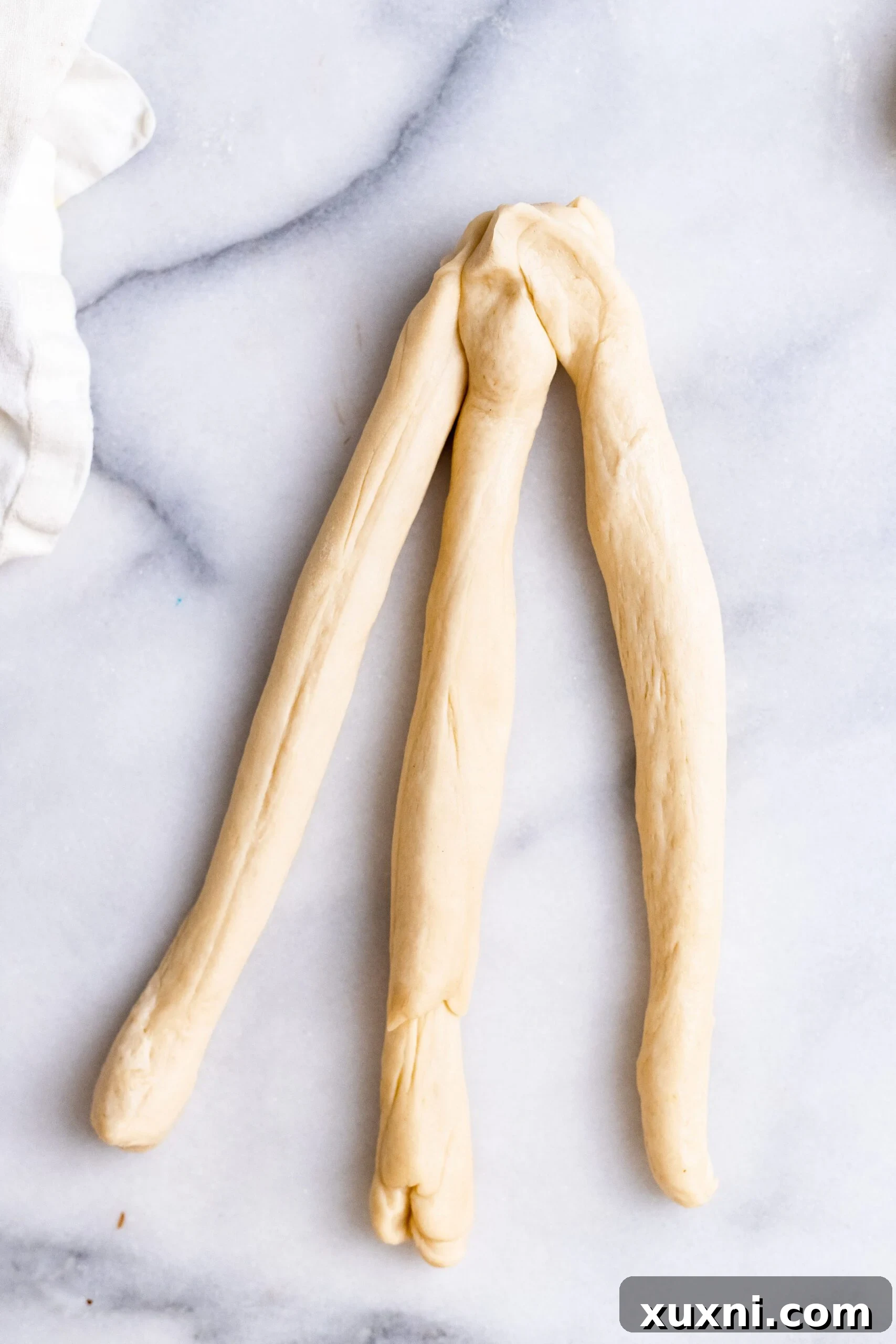 An overhead view demonstrating the technique for braiding three strands of vegan Easter bread dough.