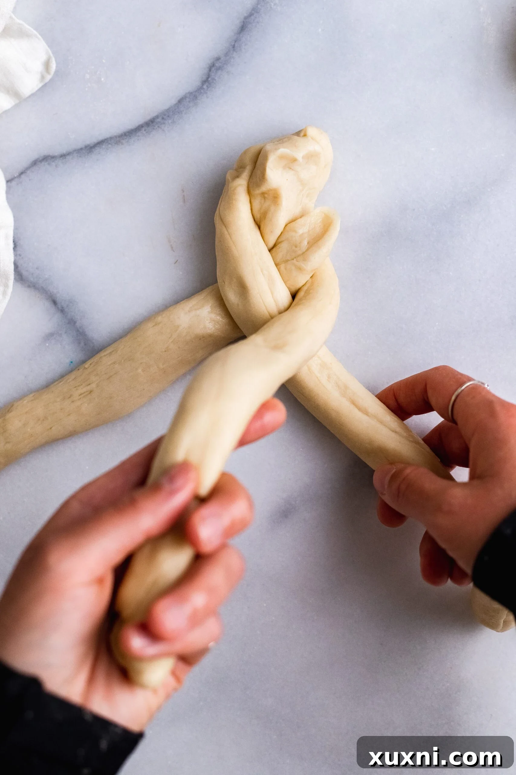 Hands carefully braiding the three strands of vegan Easter bread dough, forming the iconic shape.