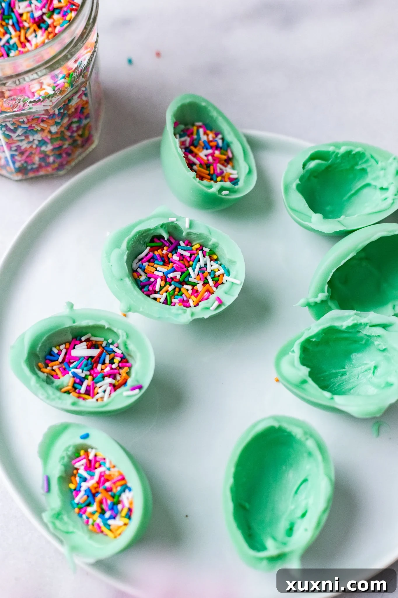 Vegan white chocolate egg halves generously filled with colorful sprinkles, poised for sealing.
