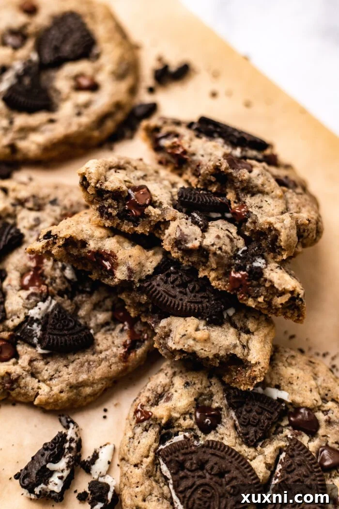 Several soft, chewy cookies and cream cookies broken into pieces, revealing the crushed Oreo chunks and melted chocolate chips within, arranged on parchment paper.