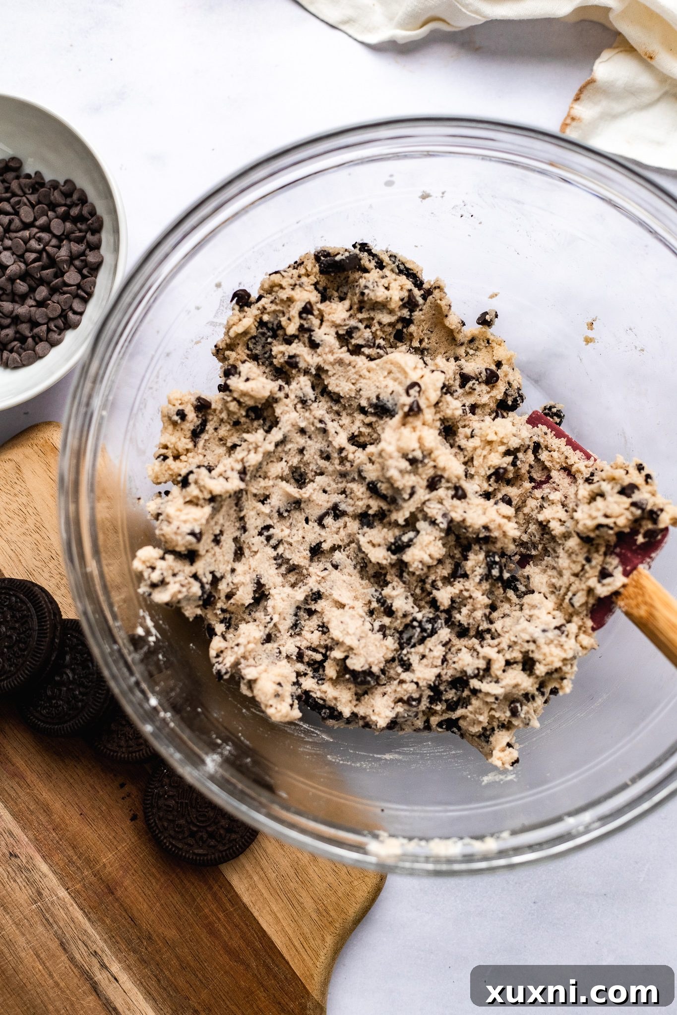 Close-up of vegan Oreo chocolate chip cookie dough in a mixing bowl, showing the chunks of crushed Oreos and chocolate chips before baking.