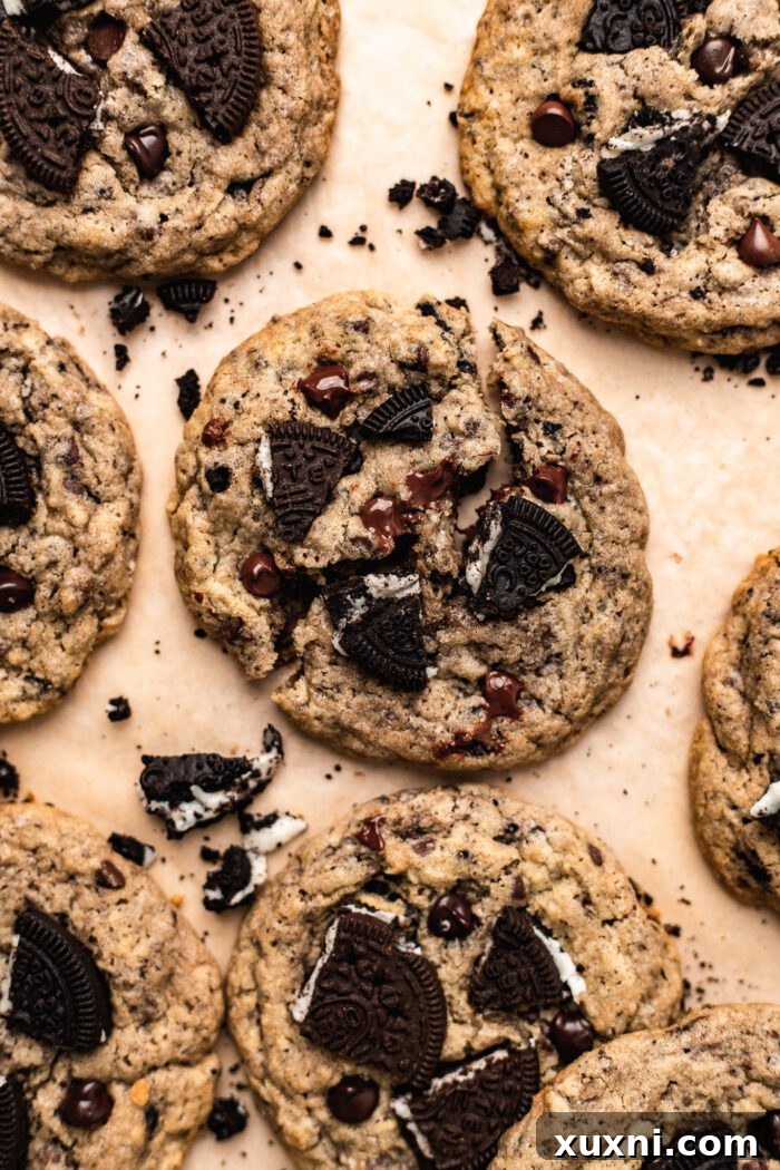 A close-up of a broken vegan Oreo chocolate chip cookie, showcasing its soft, moist interior filled with crushed Oreos and melted chocolate, on parchment paper.