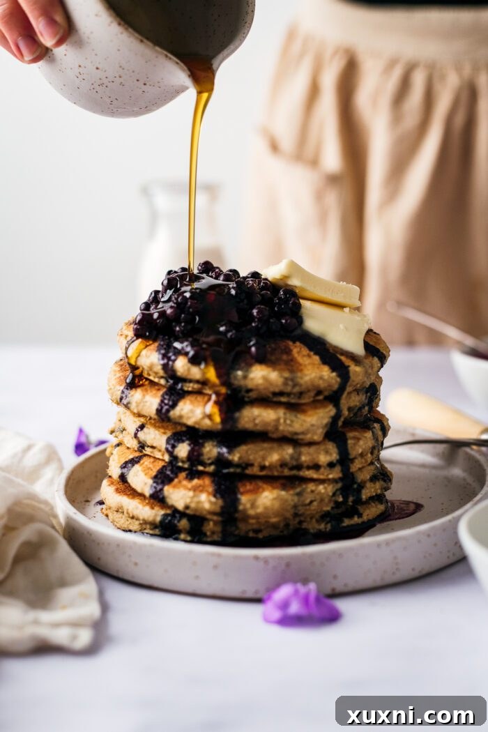 vegan oat flour pancakes with maple syrup being poured on them