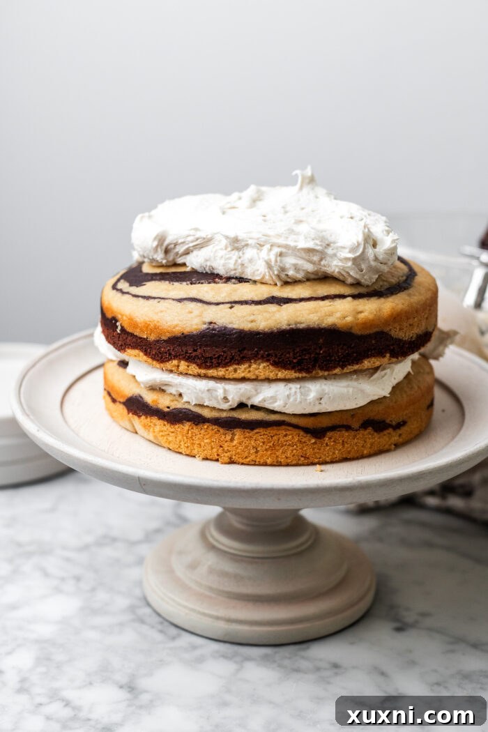 A vegan zebra cake being frosted with smooth, white cream cheese frosting.