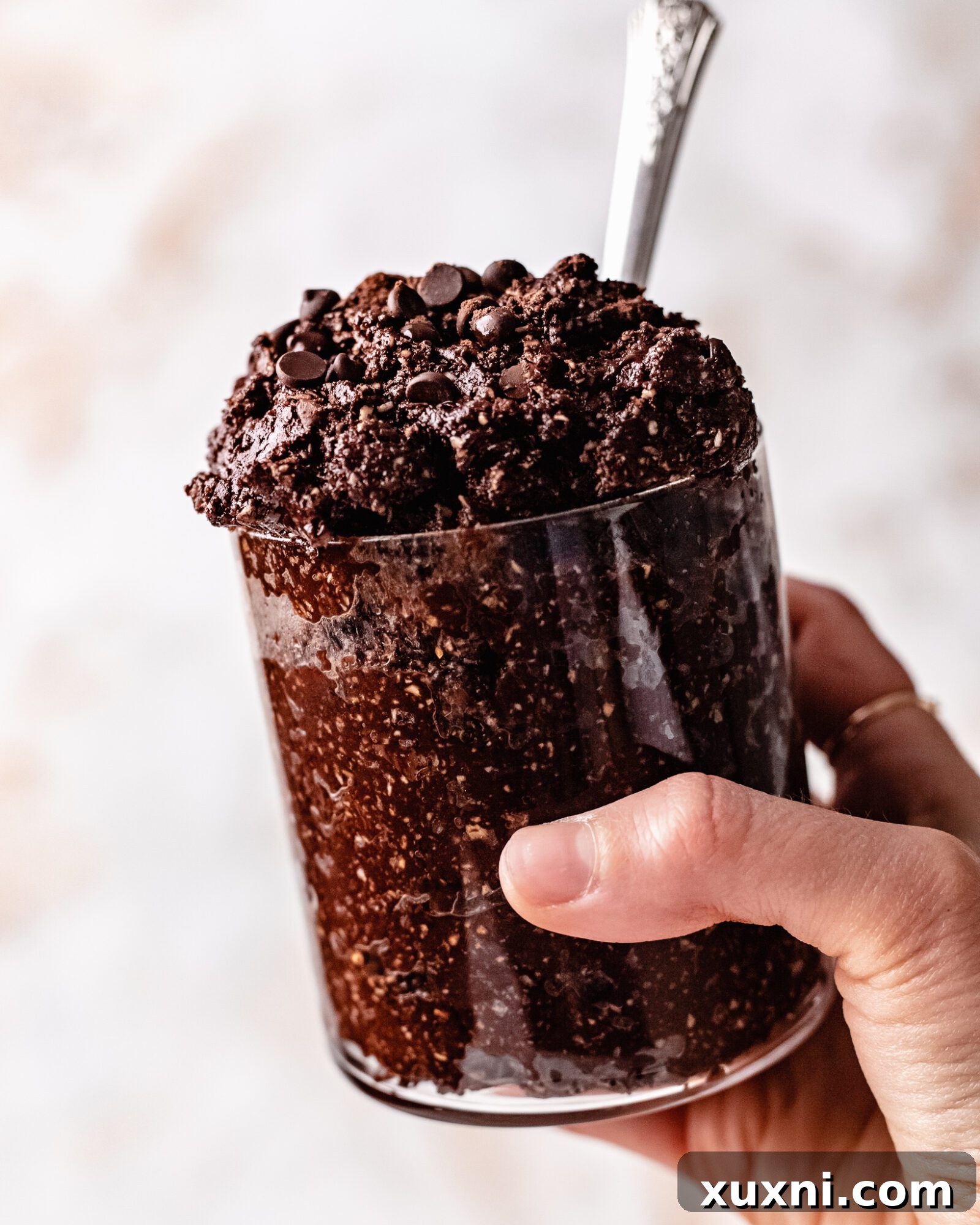 A hand holding a small cup filled with rich, healthy edible brownie batter, ready for a delicious bite.