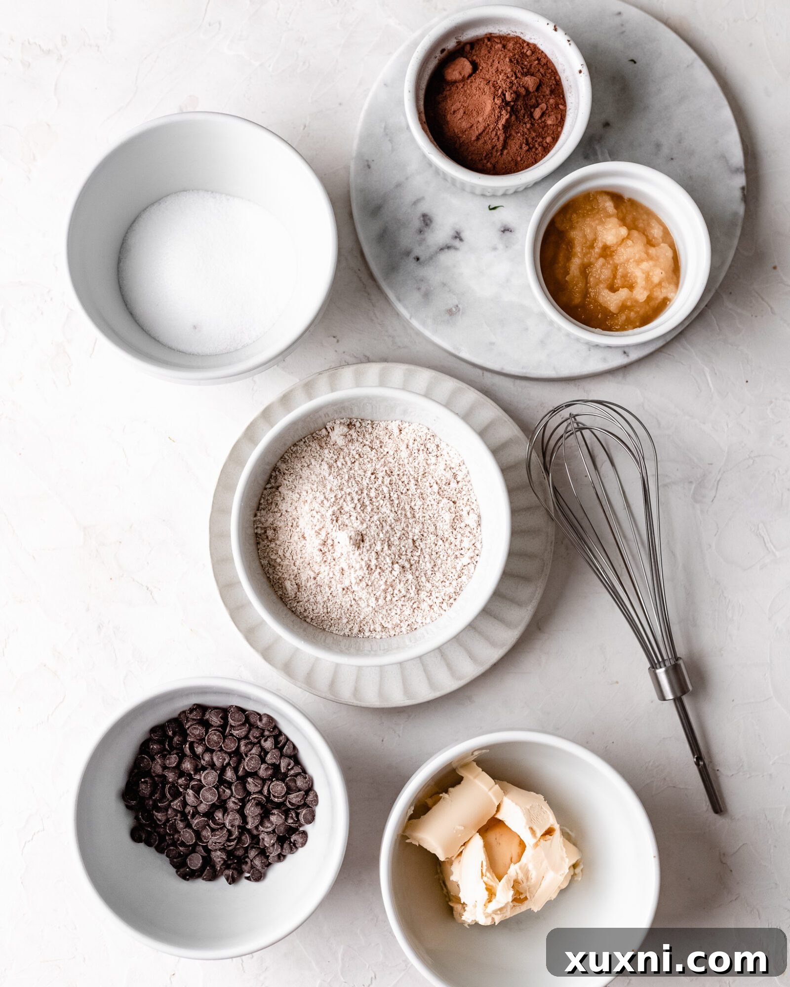 A flat lay image showing all the simple ingredients for the healthy edible brownie batter: oats, cocoa powder, vegan butter, applesauce, coconut sugar, and vegan chocolate chips.