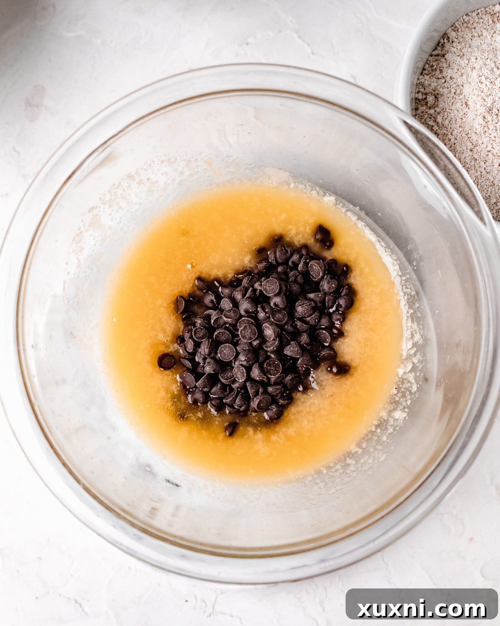 Melted vegan butter with a handful of vegan chocolate chips waiting to be stirred in, in a microwave-safe bowl.
