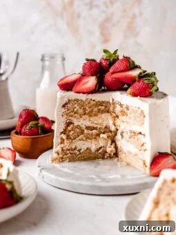 A perfectly sliced vegan sponge cake, showcasing the layers of cake and frosting, garnished with fresh strawberries.