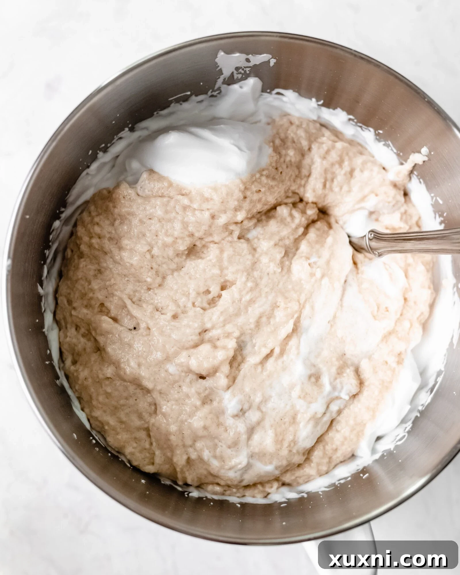 Vegan chiffon cake batter being gently folded into whipped aquafaba meringue in a large bowl.