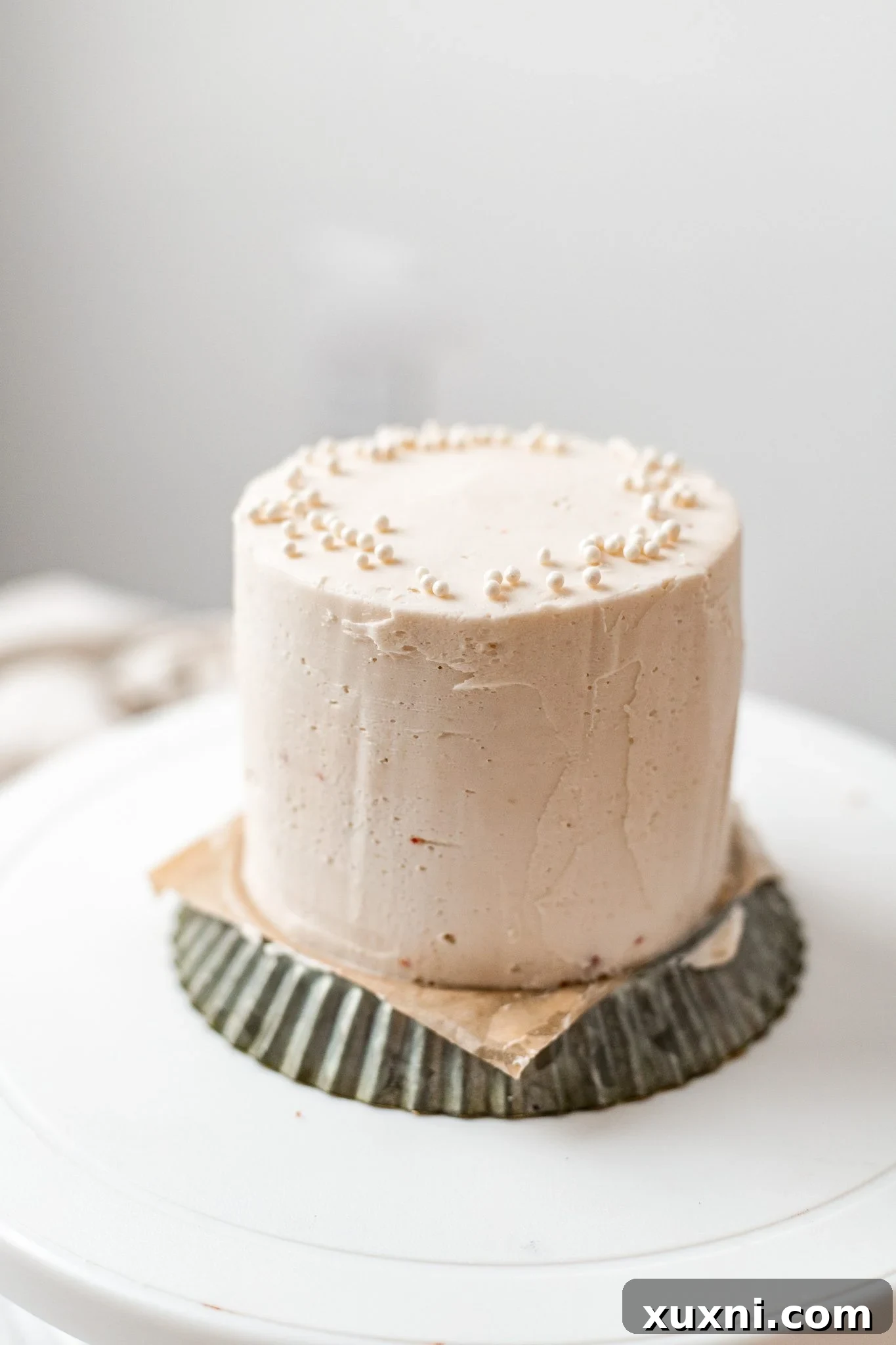 A mini cake being crumb-coated with vegan buttercream frosting on a turntable.