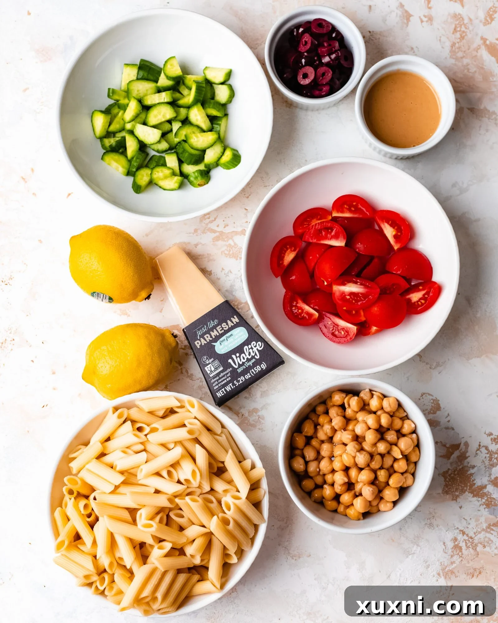 pasta salad ingredients - Fresh and colorful ingredients for a vegan pasta salad laid out: pasta, tomatoes, cucumbers, olives, chickpeas, and tahini dressing components.
