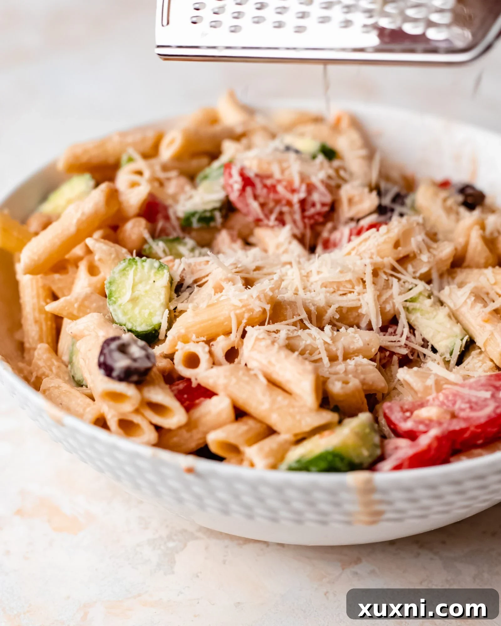 grated parmesan over healthy pasta salad - Grated vegan parmesan cheese sprinkled generously over the creamy vegan pasta salad.