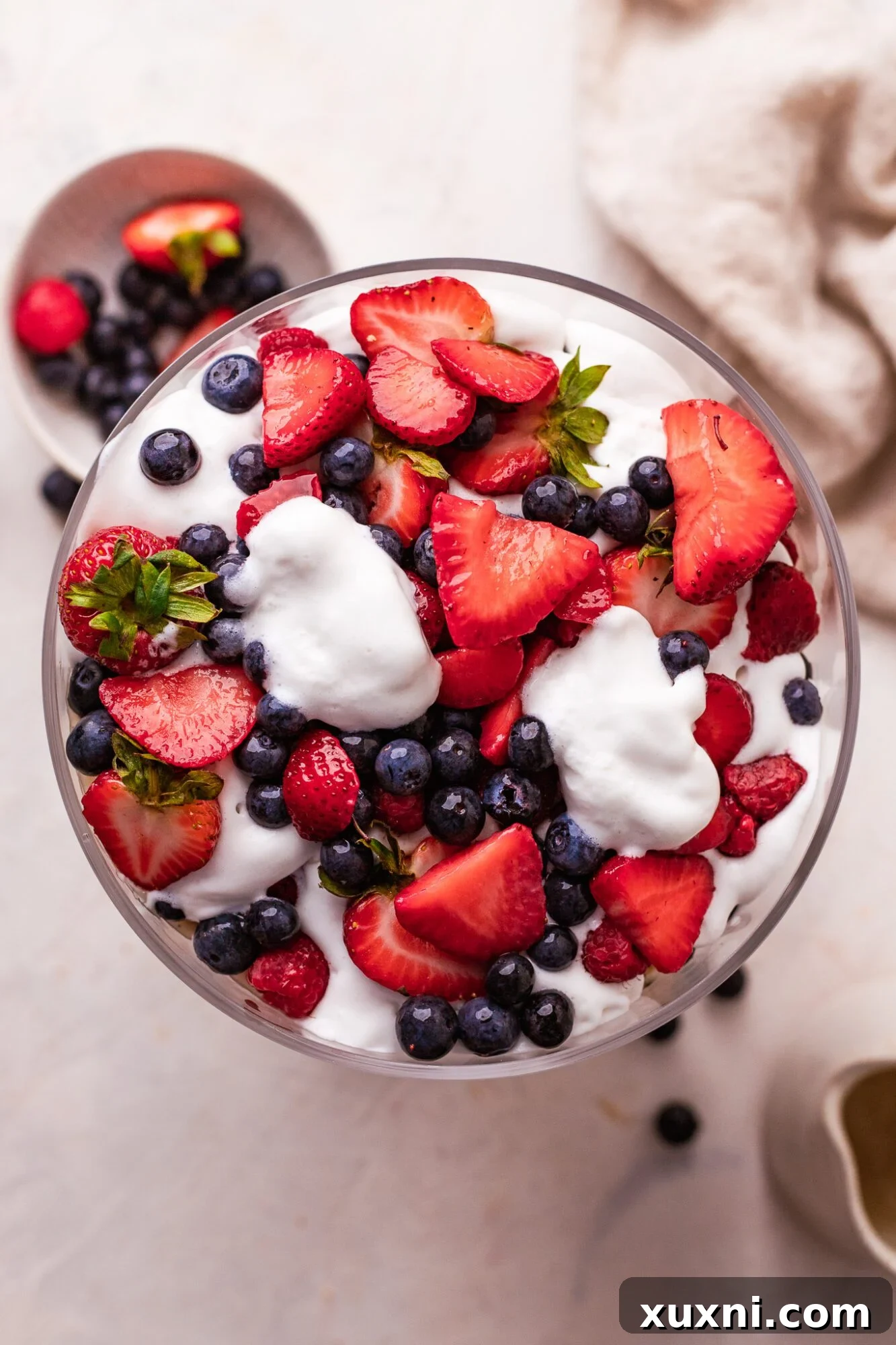 Close-up of a glass trifle dish showcasing the vibrant layers of vegan lemon custard, fresh berries, and vanilla pound cake.