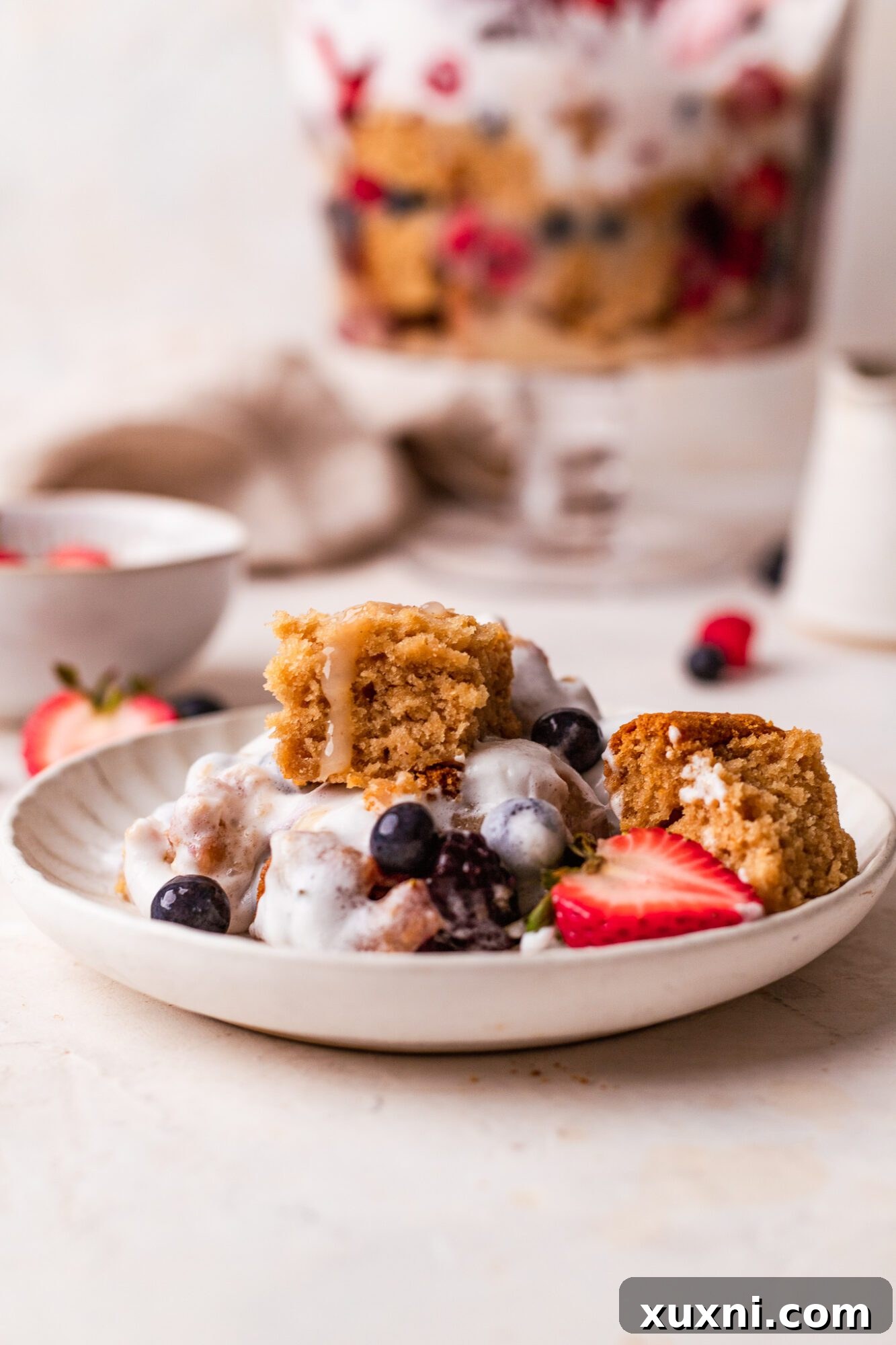A single serving of vegan lemon berry trifle on a white plate, showing the beautiful layers, topped with berries.