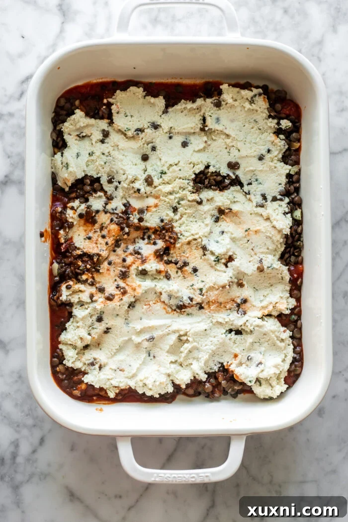 Hands assembling the layers of vegan lasagna in a baking dish