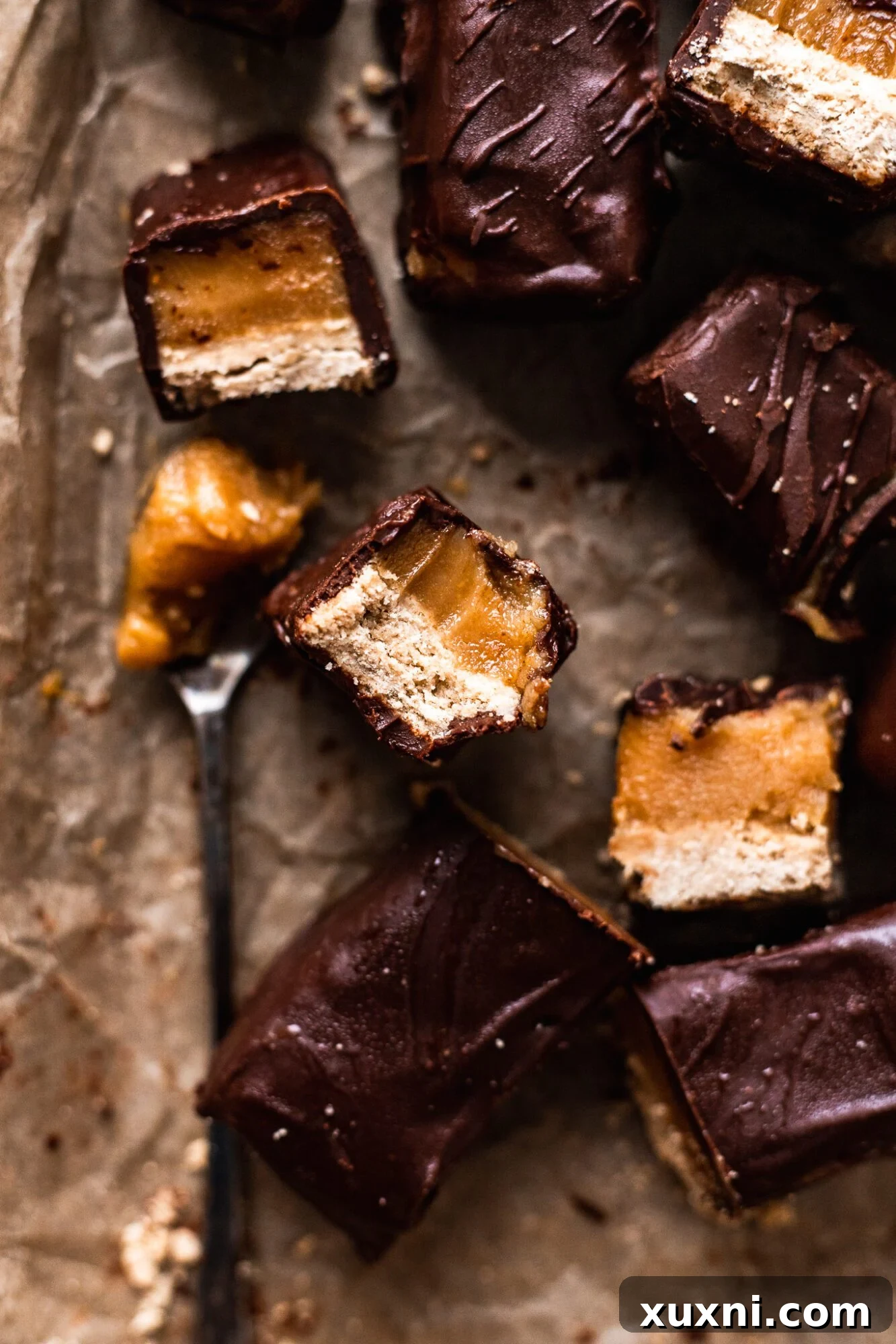 Homemade vegan Twix bars artfully arranged, showcasing layers of shortbread, caramel, and chocolate.