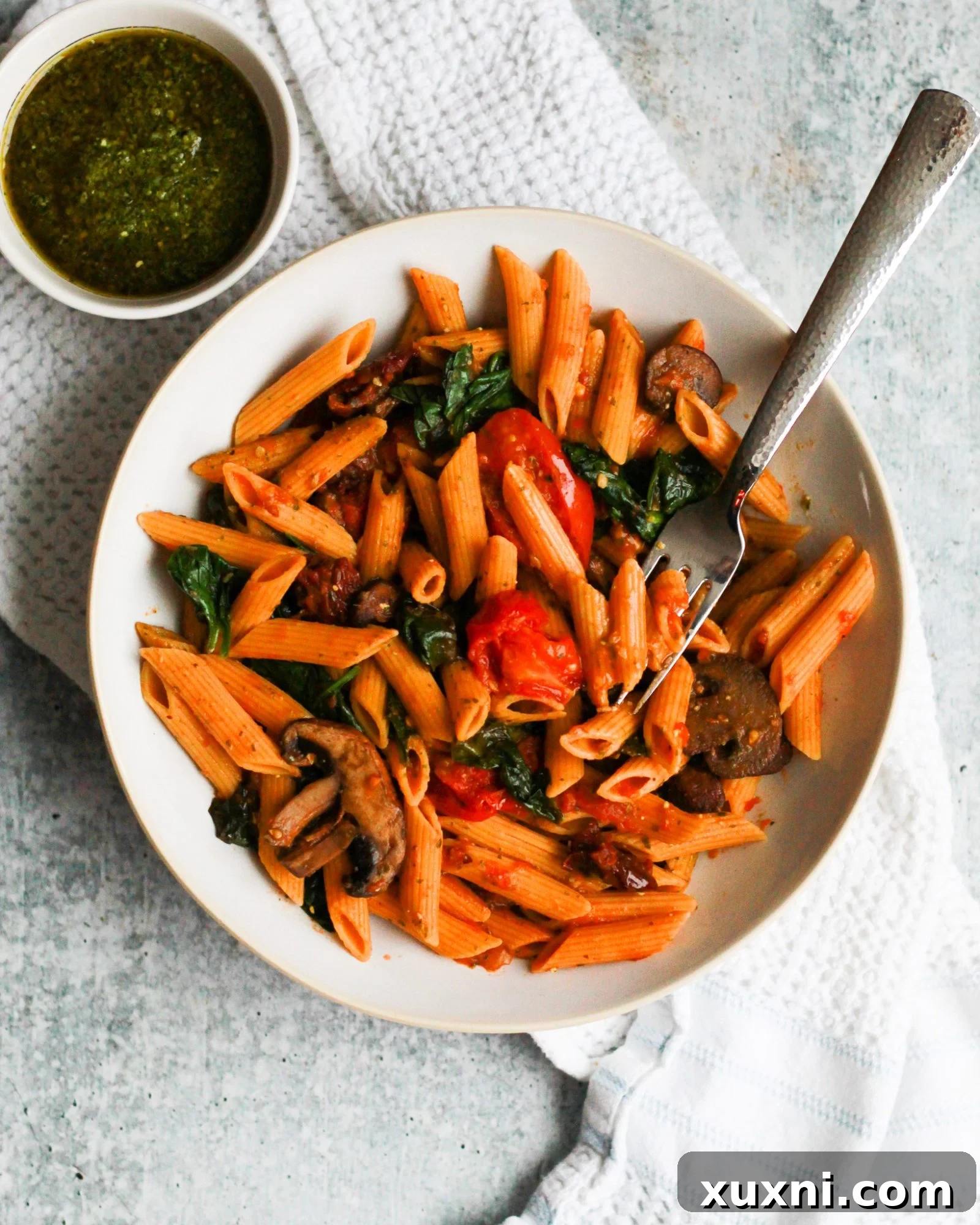 A large serving of vegan sun-dried tomato pesto pasta, showing the mix of pasta, rich sauce, and colorful vegetables in a bowl.