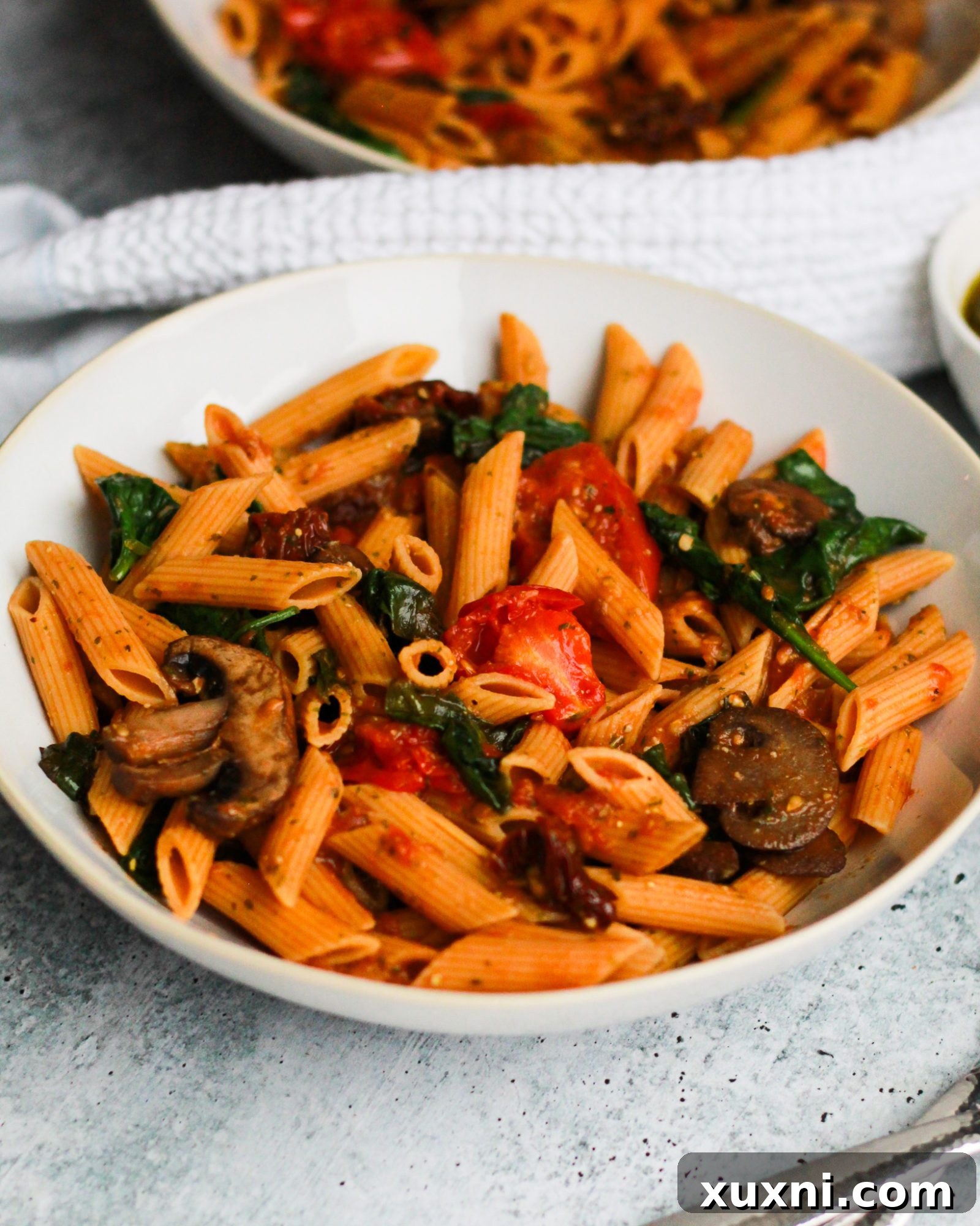 Close-up shot of a fork lifting a twirl of vegan sun-dried tomato pesto pasta, perfectly coated in sauce and interspersed with veggies.