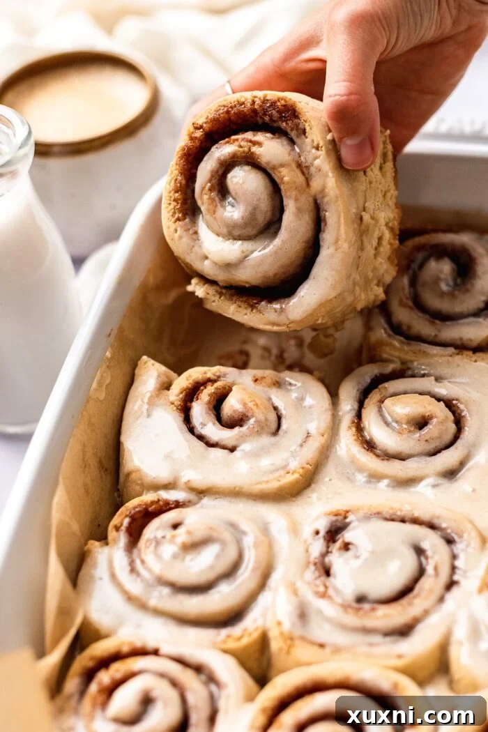 hand grabbing gluten free vegan cinnamon roll from baking pan