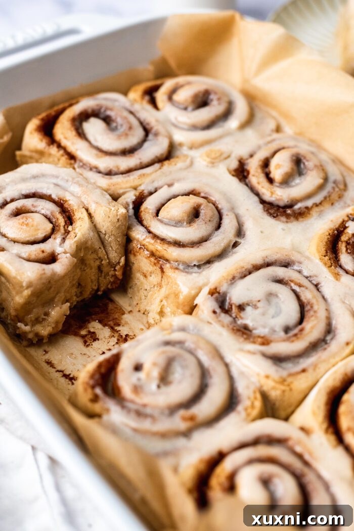baked gluten free cinnamon rolls with icing on top in baking pan with parchment paper