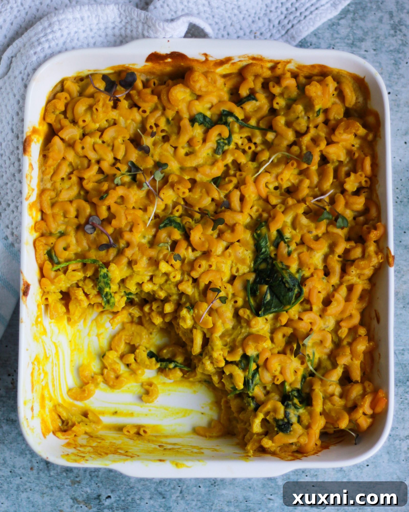 A baking dish of vegan mac and cheese with a portion scooped out, highlighting its tempting texture.