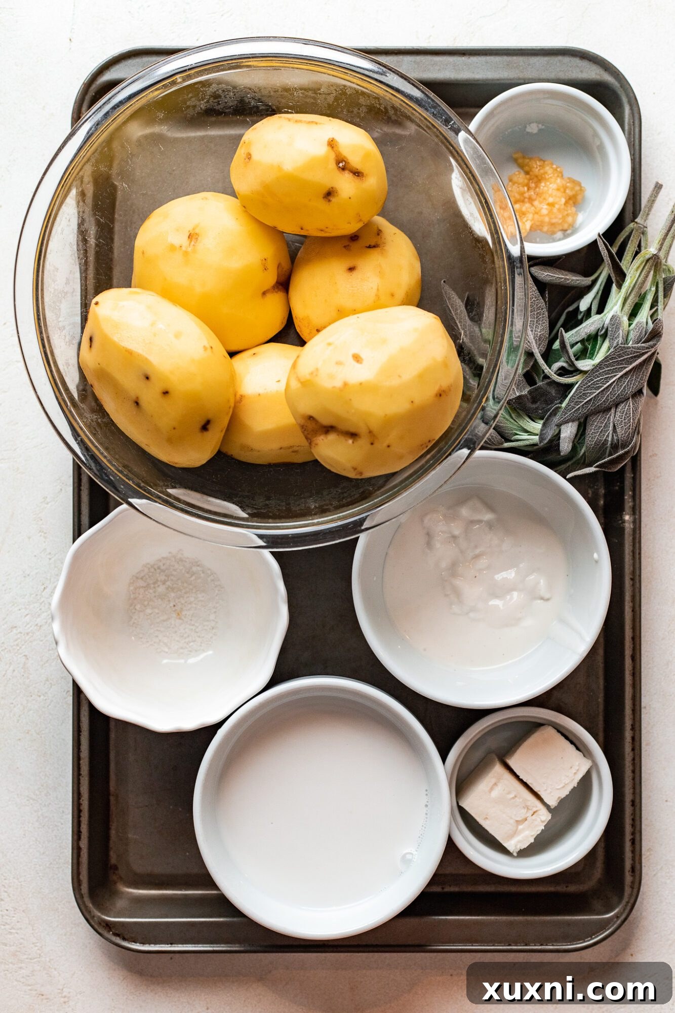 Fresh ingredients laid out for making vegan mashed potatoes, including Russet and Yukon Gold potatoes, vegan sour cream, and rosemary.