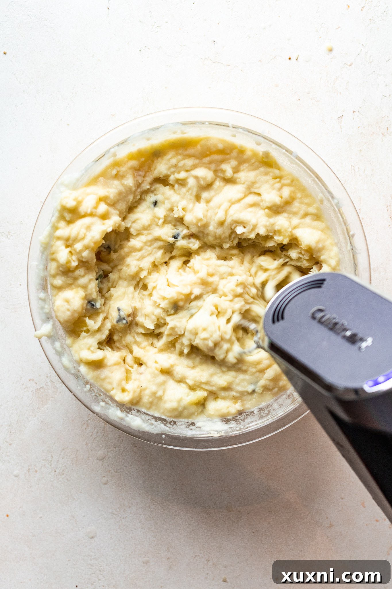Using a hand mixer to create perfectly smooth and creamy vegan mashed potatoes, a key step for ultimate fluffiness.