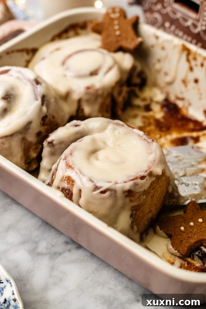A single gingerbread cinnamon roll, still warm, in a casserole dish, topped with generous frosting.