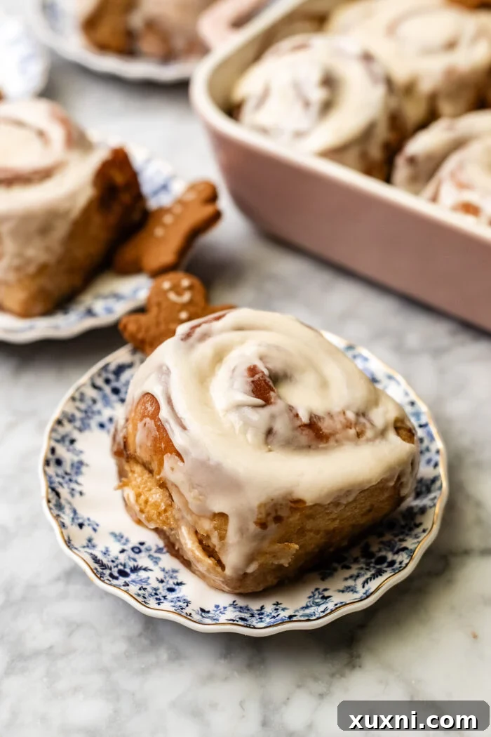 A beautifully frosted gingerbread cinnamon roll on a plate, ready to be eaten.