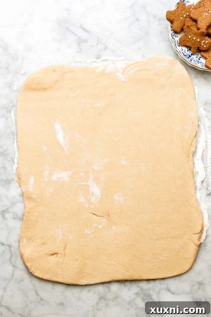 Gingerbread cinnamon roll dough rolled out into a large square on a floured surface.
