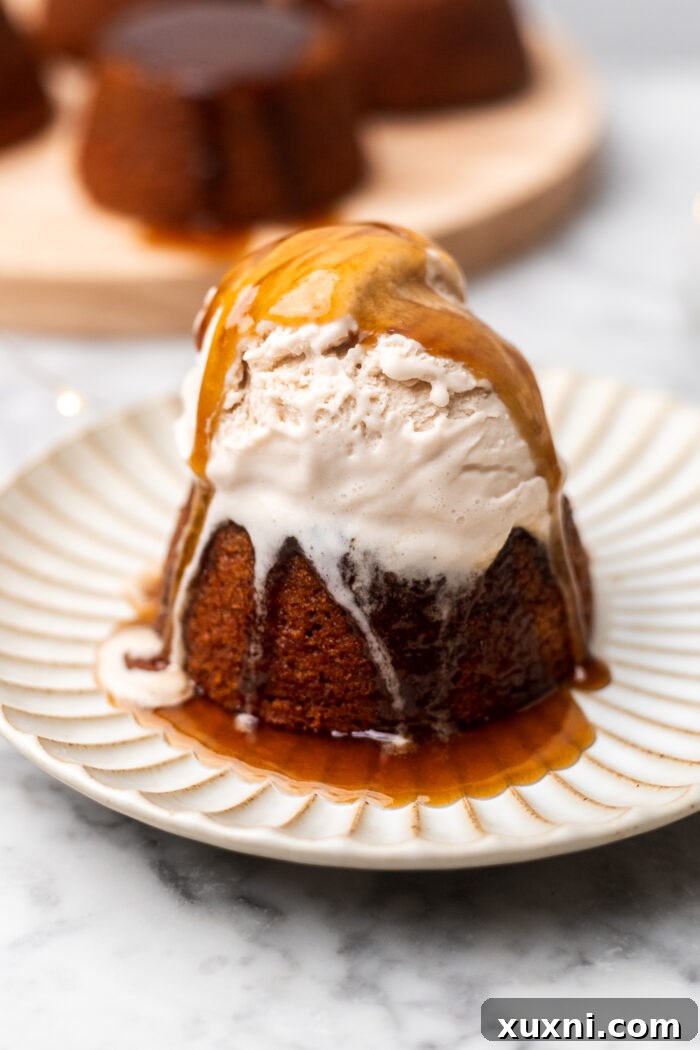 Simply Divine Vegan Sticky Toffee Pudding 12 A single serving of vegan sticky toffee pudding on a plate, topped with a scoop of vegan vanilla ice cream and more sauce.