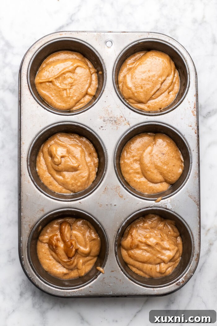 Simply Divine Vegan Sticky Toffee Pudding 7 Muffin tin with a spoonful of toffee sauce at the bottom of each cup, ready for the pudding batter.