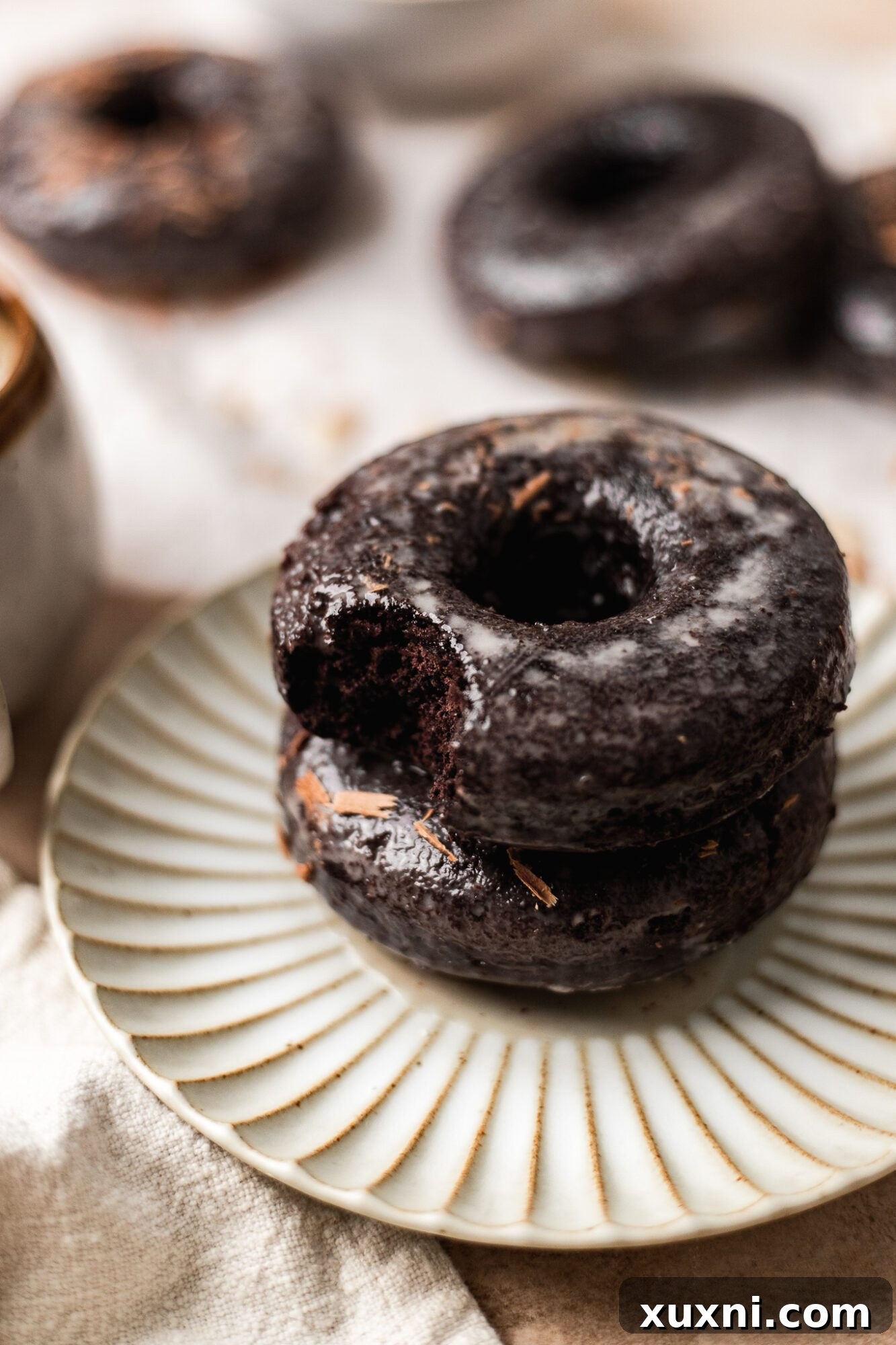 A stack of three beautifully glazed vegan chocolate donuts, showcasing their rich color and smooth glaze.